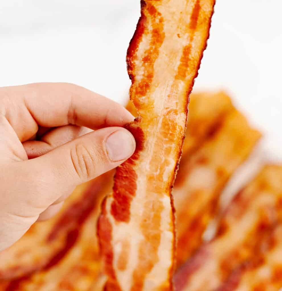 Hand Holding Crispy Bacon with More Bacon in the Background