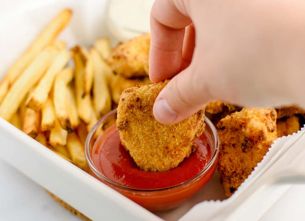 Dipping Nugget Into Ketchup with Fries in Background