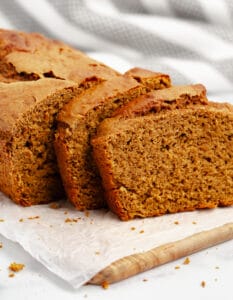 Pumpkin Bread Sliced on Wooden Board and Parchment and Stripe Towel in Background