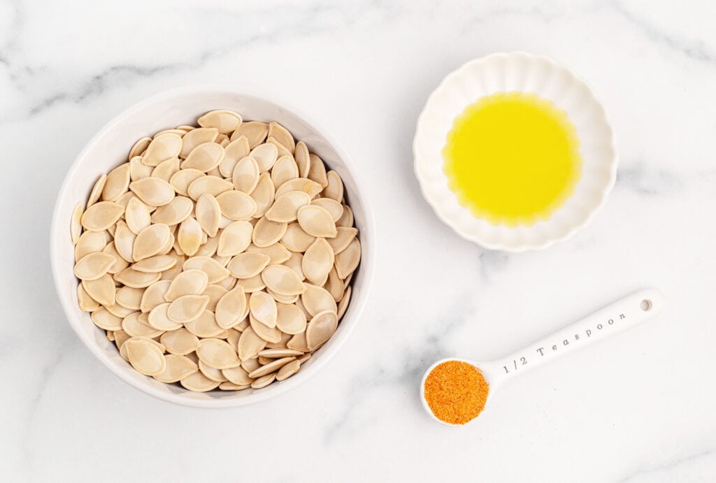 Pumpkin Seeds, Olive Oil, and Seasoning in Bowls on White Countertop