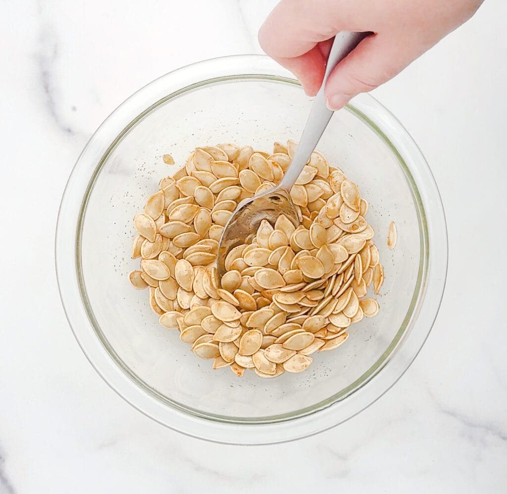 Mixing Pumpkin Seeds, Oil, Seasonings in Bowl with Spoon