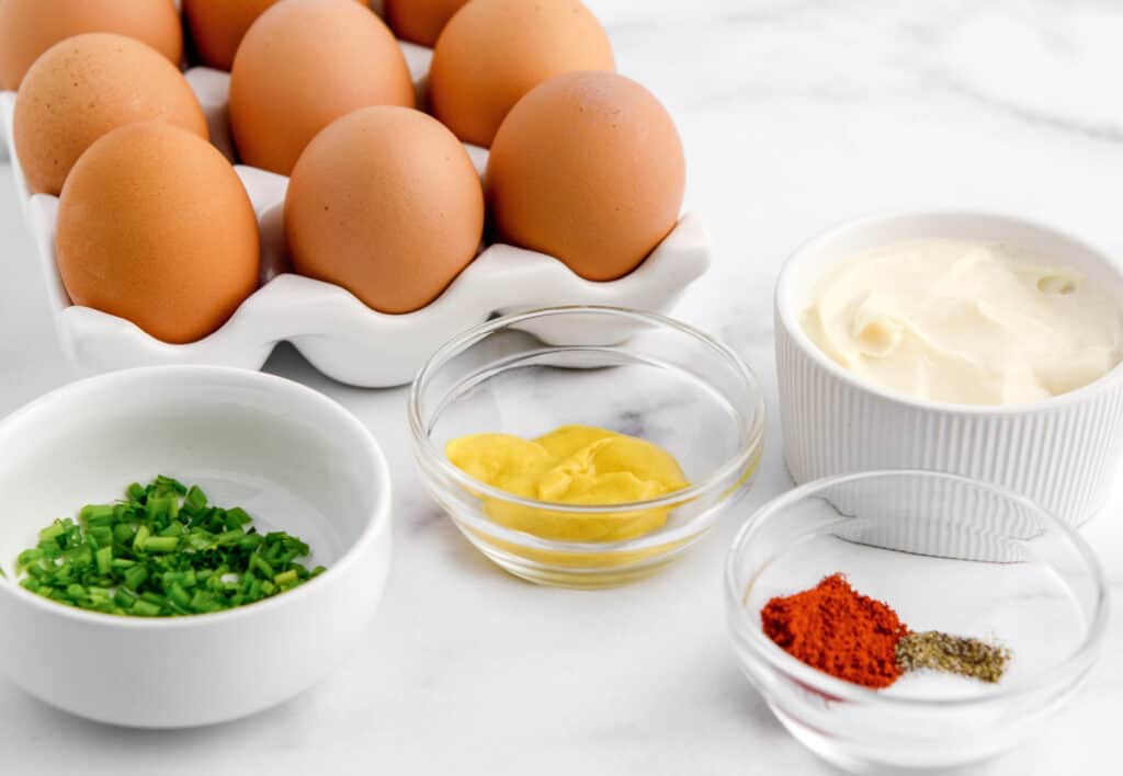 Ingredients for Deviled Eggs Including Eggs, Miracle Whip, Mustard, Chives, Salt, Pepper, and Paprika in Bowls