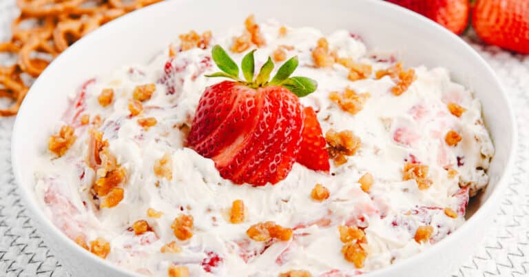 Strawberry Pretzel Salad in a White Serving Bowl with a Sliced Fresh Strawberry and Sugared Pretzels on Top