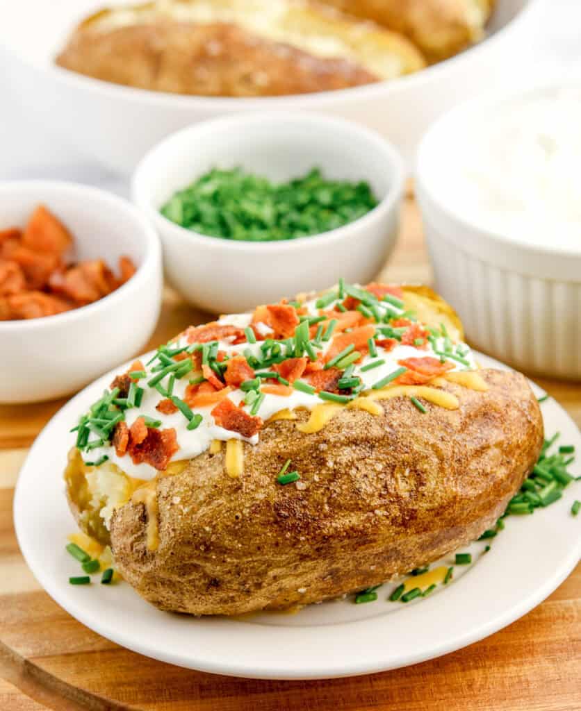 Baked Potato with Toppings on Plate with Bowls of Toppings in the Background