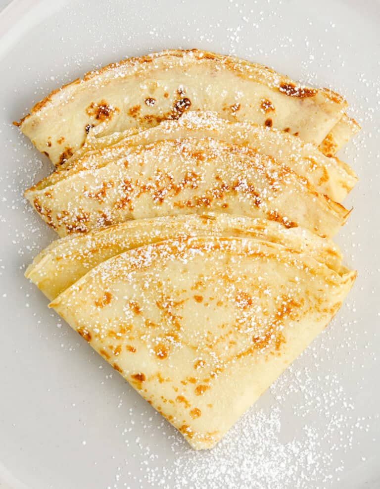 3 Folded Crepes Dusted with Powdered Sugar on a Plate