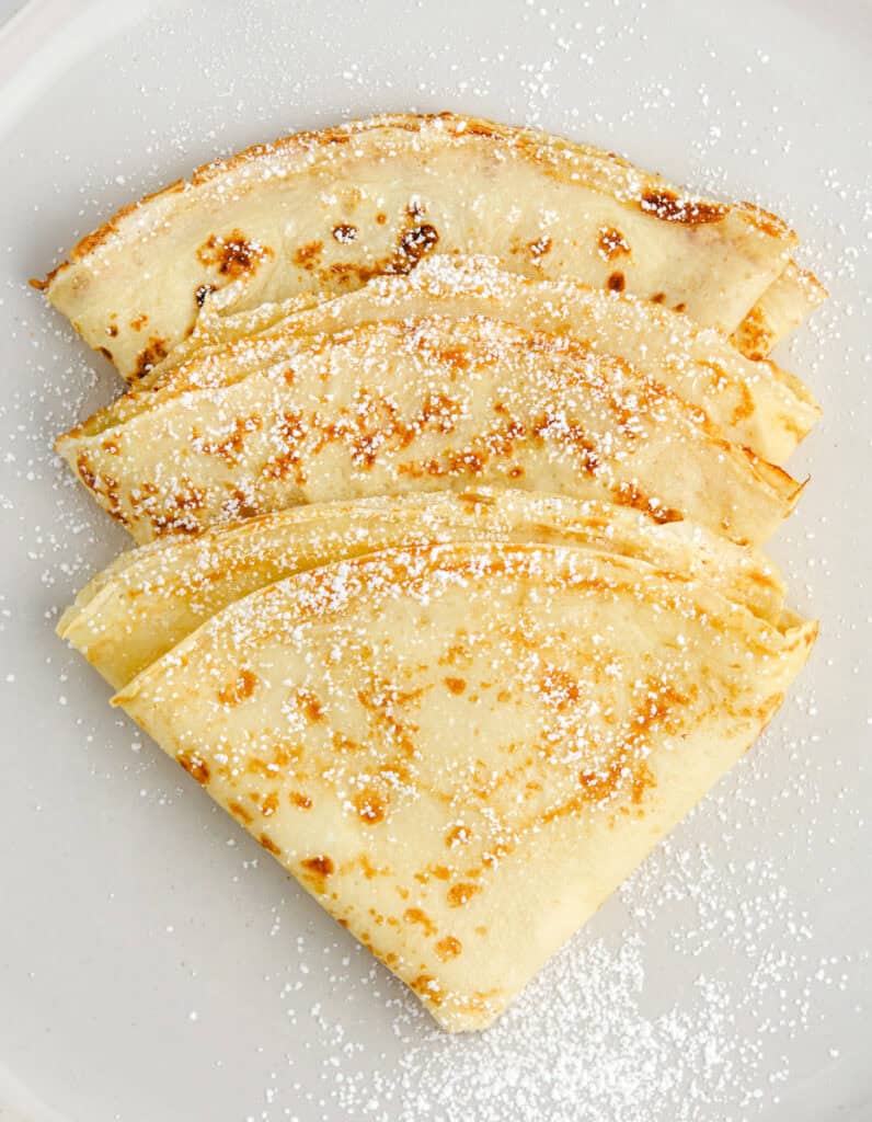 3 Folded Crepes Dusted with Powdered Sugar on a Plate