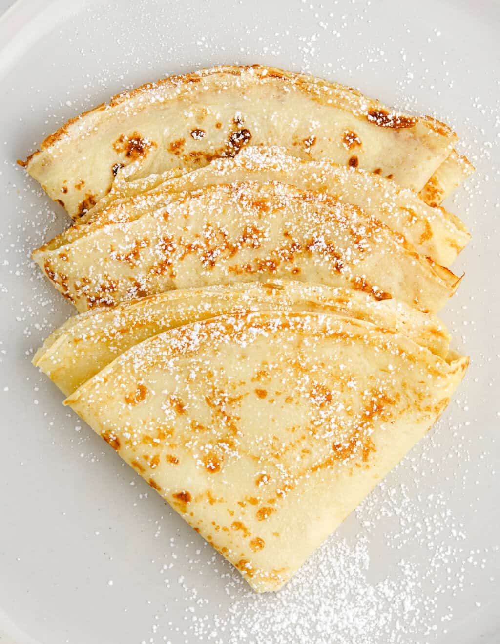 3 Folded Crepes Dusted with Powdered Sugar on a Plate