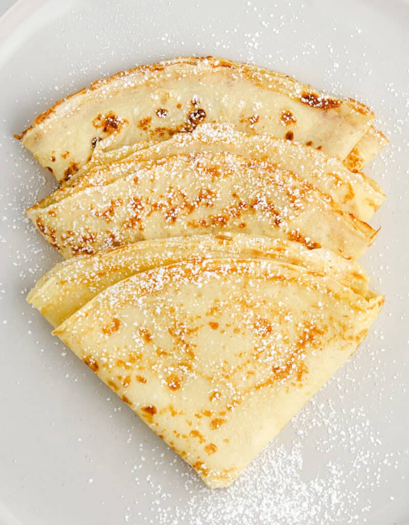 Three Crepes Folded and Dusted with Powdered Sugar on a Plate