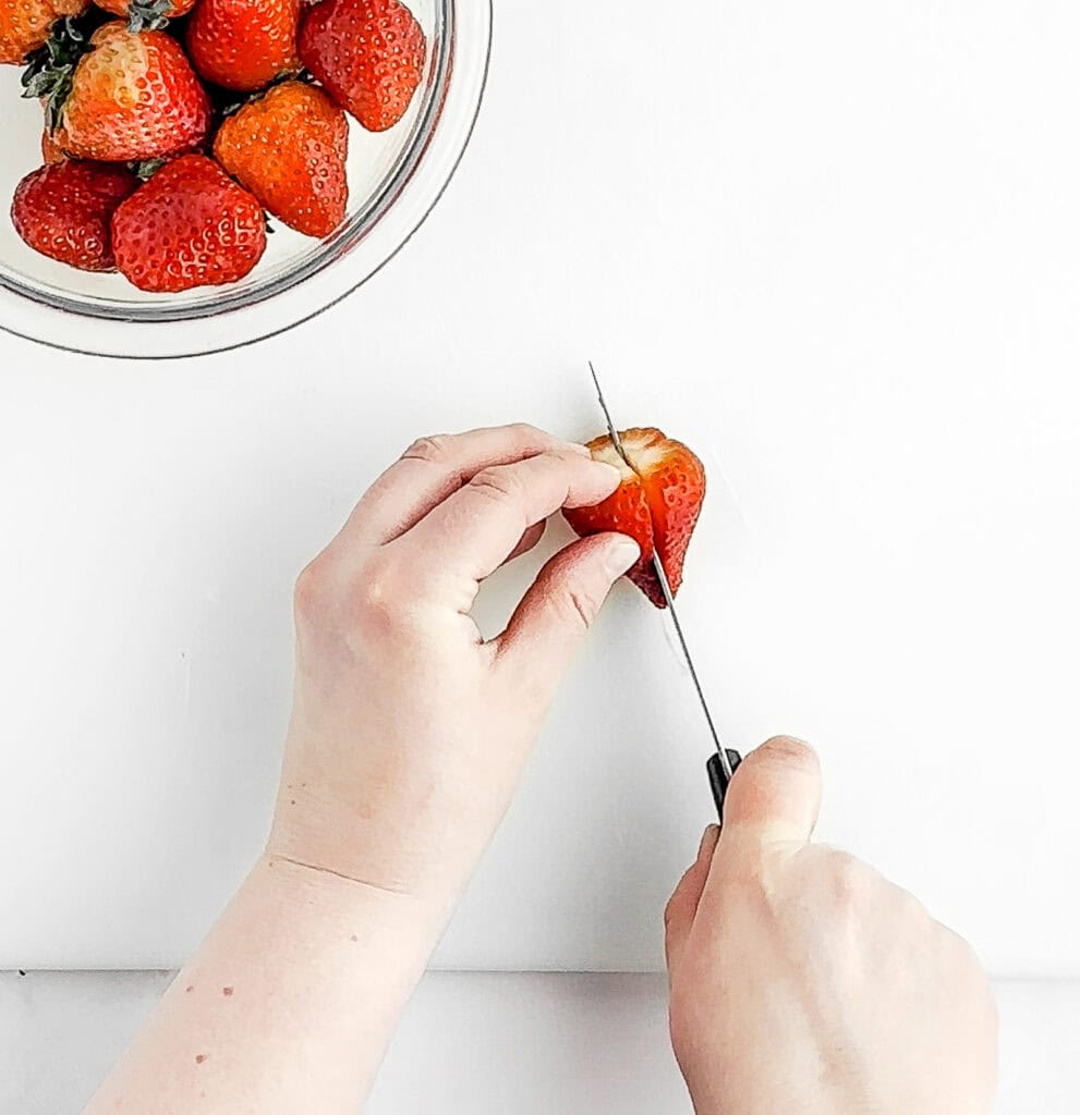 Slicing a Strawberry in Half with Bowl of Strawberries in the Back
