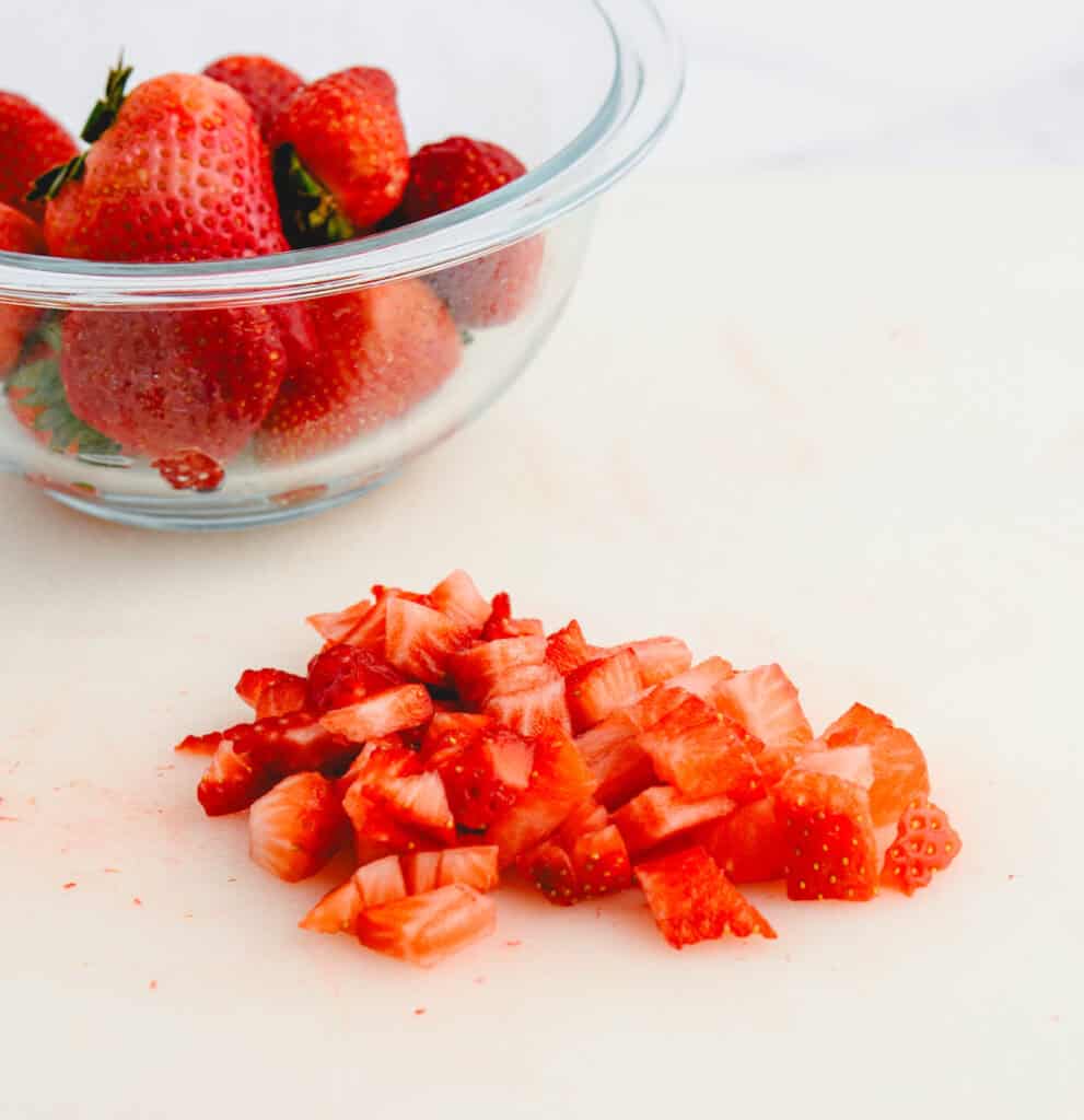 Diced Strawberries on Cutting Board with Whole Strawberries in a Bowl