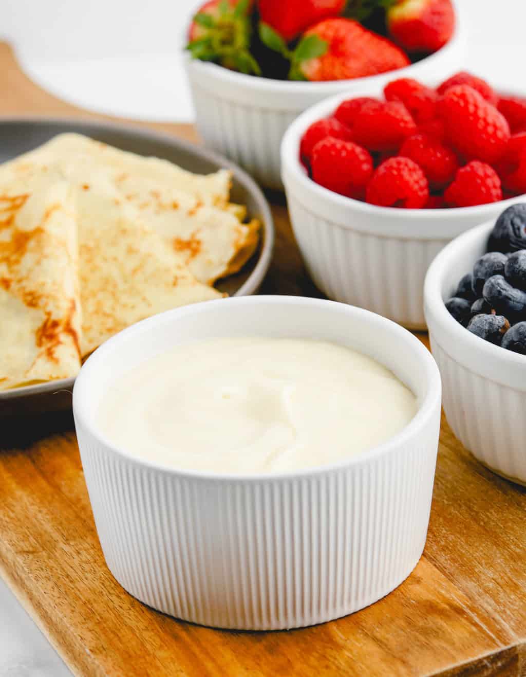 Sweet Cream Cheese Crepe Filling in Bowl with Berries and Crepes in the Background